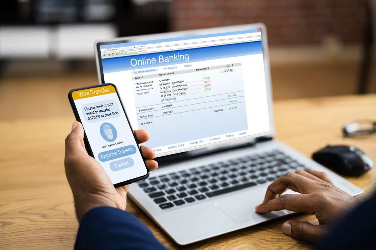 uomo con smartphone in mano e pc acceso su pagina web del conto bancario online