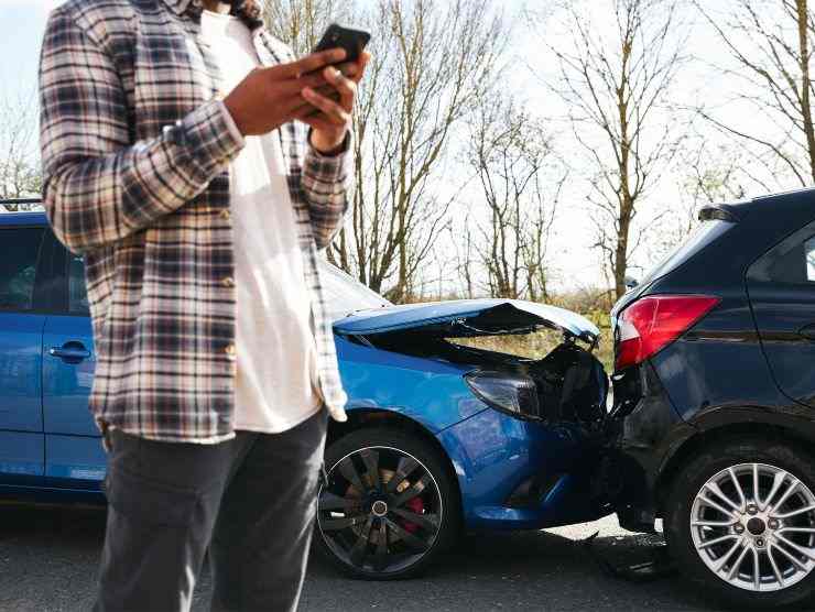uomo che usa smartphone per segnalare incidente tra due auto