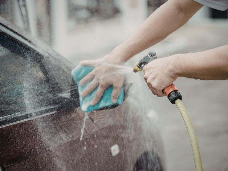 persona che lava auto con pompa e spugna
