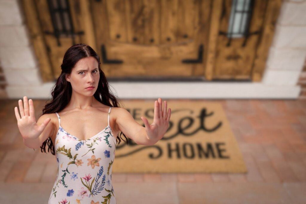 in primo piano una donna che dice no e come sfondo una porta d'ingresso con uno zerbino